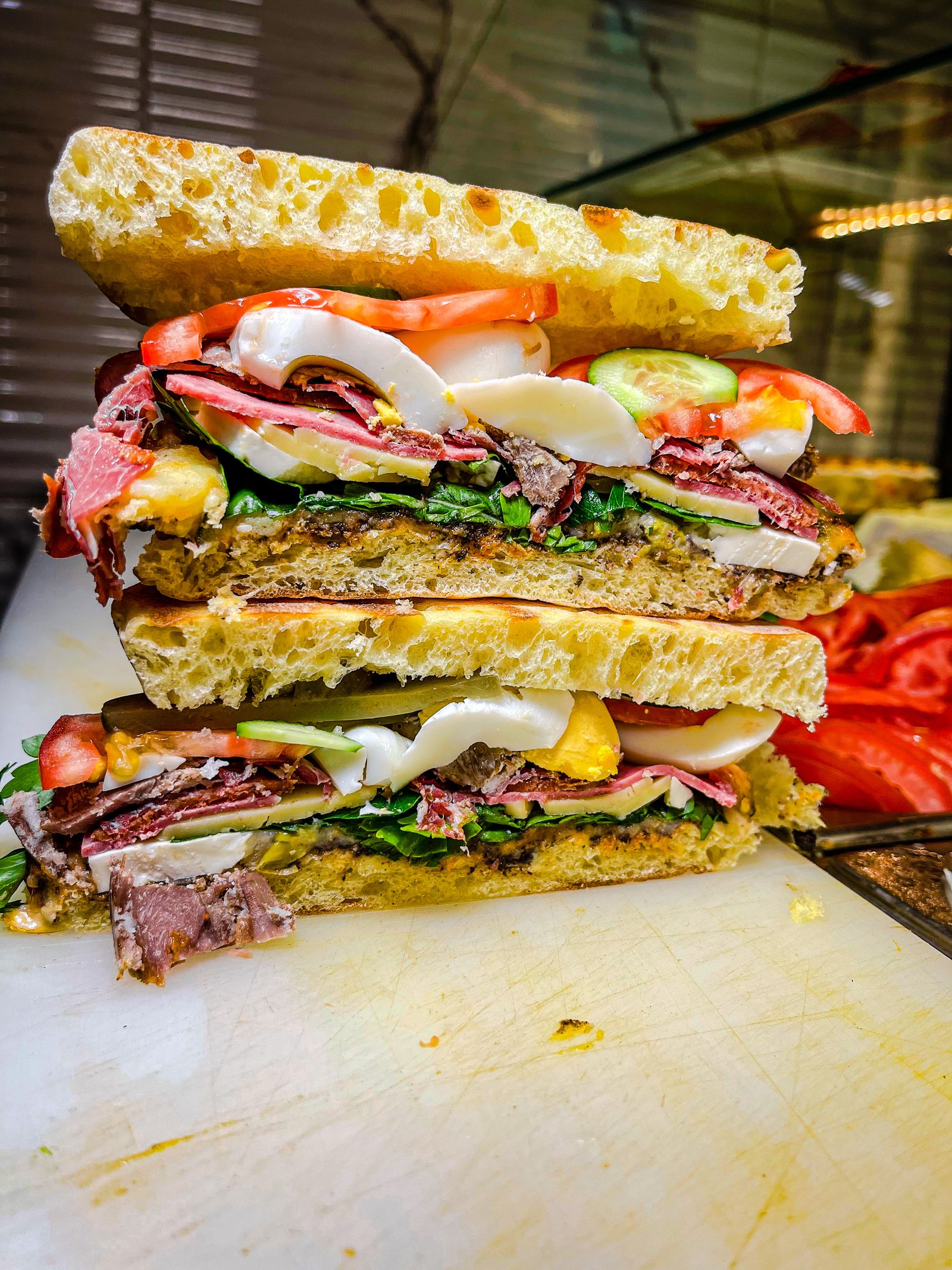 A tall stacked Italian sub layered with meats, cheese, and tomato